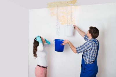 young woman standing with worker collecting water in bucket from ceiling in house