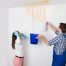 young woman standing with worker collecting water in bucket from ceiling in house